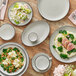 A gray matte stoneware cup with a handle, shown on a matching saucer among various plates of food.