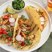 A plate of tacos with chicken, radishes, and lime with a bowl of cilantro.