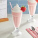 A glass of pink milkshake with a straw and a strawberry on top.