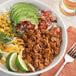 A bowl of taco meat with avocado and lime.