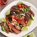 A plate of grilled steak with lime slices and tomatoes.