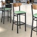 A group of Lancaster Table & Seating bar stools with green vinyl seats and vintage wood backs at a bar counter.