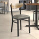 A Lancaster Table & Seating Boomerang Series chair with a dark gray vinyl cushion next to a table in a restaurant.