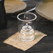 A Sterno Petite Clear Votive Glass with a lit candle inside on a table.