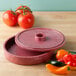A red round HS Inc. polyethylene container with a lid on a table with tomatoes.