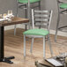 A Lancaster Table & Seating Ladder Back chair with a seafoam vinyl cushion sits next to a table in a restaurant.