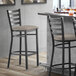 A Lancaster Table & Seating black finish ladder back bar stool with dark gray vinyl padded seat.