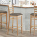 Three Lancaster Table & Seating wooden bar stools with taupe vinyl seats at a counter.