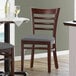 A Lancaster Table & Seating wood ladder back chair with a dark gray vinyl seat next to a table.