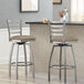 Two Lancaster Table & Seating ladder back swivel bar stools with taupe vinyl padded seats at a counter.