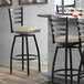 A Lancaster Table & Seating black finish ladder back swivel bar stool with light gray vinyl padded seat at a table.