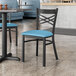 A blue cushioned Lancaster Table & Seating Black Cross Back Chair at a table in a restaurant.