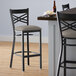 A Lancaster Table & Seating black cross back bar stool with a dark gray cushion next to a table.