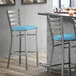 A Lancaster Table & Seating clear coat finish ladder back bar stool with a blue vinyl padded seat.