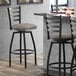 A Lancaster Table & Seating black finish ladder back swivel bar stool with a dark gray vinyl padded seat next to a table.