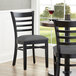 A Lancaster Table & Seating black wood ladder back chair with a dark gray vinyl seat at a restaurant table.