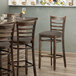 A Lancaster Table & Seating wood ladder back bar stool with taupe vinyl seats at a table in a restaurant.
