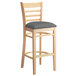 A Lancaster Table & Seating wooden bar stool with a dark gray cushion on the seat.