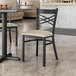 A Lancaster Table & Seating black cross back chair with a light gray cushion on a table in a restaurant.