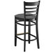 A black Lancaster Table & Seating wooden ladder back bar stool with a dark gray cushion.