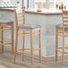 Three Lancaster Table & Seating wooden bar stools with light gray vinyl seats at a counter.