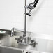 A white wall with a stainless steel Equip by T&S pre-rinse faucet above a sink.