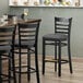 A Lancaster Table & Seating black wood ladder back bar stool with a dark gray vinyl seat.