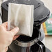 A person's hand holding a Folgers Classic Decaf 4-cup coffee filter pack over a coffee maker.