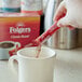 A person pouring Folgers Classic Roast instant coffee into a white mug.