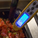A Taylor digital pocket probe thermometer taking the temperature of diced tomatoes.