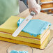 A person's hand using a Choice 12" straight baking / icing spatula to cut a cake