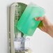 A hand pouring Dial Hypoallergenic Liquid Hand Soap into a green soap dispenser.