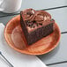 A piece of chocolate cake with frosting on a Choice woven wood plate.