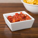 A CAC China white square bowl filled with salsa next to a bowl of chips.