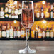 An Anchor Hocking Florentine II flute glass filled with pink champagne on a table in a bar.