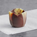 A Mona Lisa marbled chocolate tulip cup filled with chocolate on a white surface.