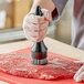 A person using a Choice 20-prong meat tool to tenderize meat on a butcher shop counter.