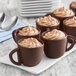 A group of Mona Lisa mini chocolate coffee cups filled with brown liquid and topped with whipped cream on a counter.