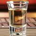 An Anchor Hocking tequila shot glass filled with liquid on a table.