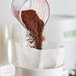 A measuring cup pours Toddy Blend Low Acid Cold Brew Coarse Ground Coffee into a paper bag.