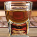 An Anchor Hocking straight sided shot glass with brown liquid in it.