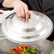 A chef using a Thunder Group aluminum wok cover to steam vegetables.