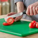 A person using a Choice Classic utility knife to cut a tomato on a green cutting board.
