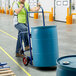 A man using a Lavex steel drum hand truck to move a blue barrel.