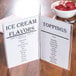 A Tablecraft menu table tent with an ice cream toppings and flavors menu on a table.