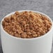 A bowl of brown granola with white cups of Cinnamon Streusel Ice Cream Topping.