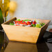 An American Metalcraft square bamboo bowl filled with salad on a table.