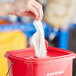 A hand pulling a white paper towel from a red bucket.