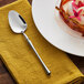 An Acopa stainless steel dessert spoon on a napkin next to a plate of dessert.