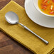 An Acopa bouillon spoon on a napkin next to a bowl of soup